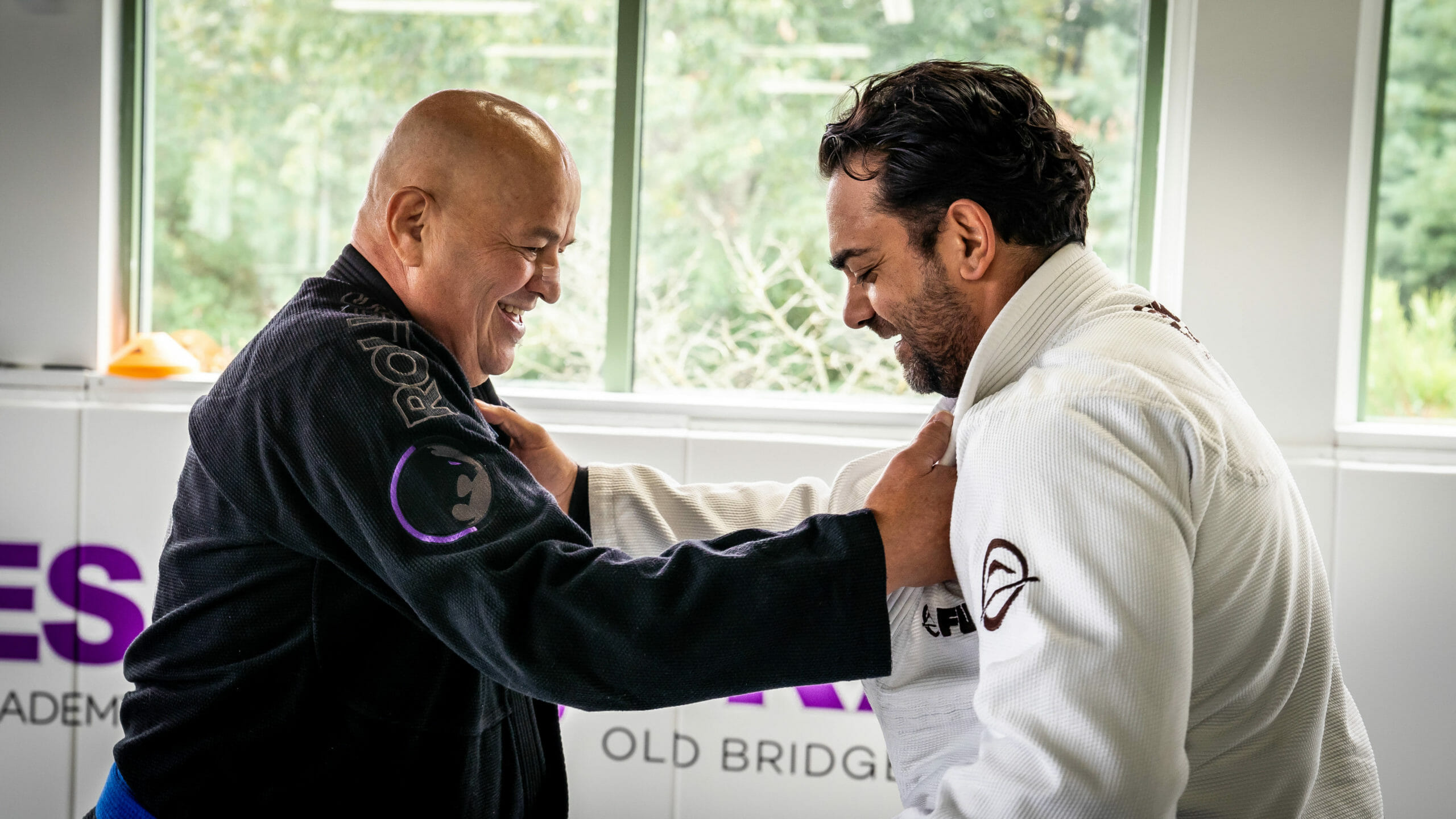 Two Brazilian Jiu-Jitsu practitioners in gis training together in a bright academy