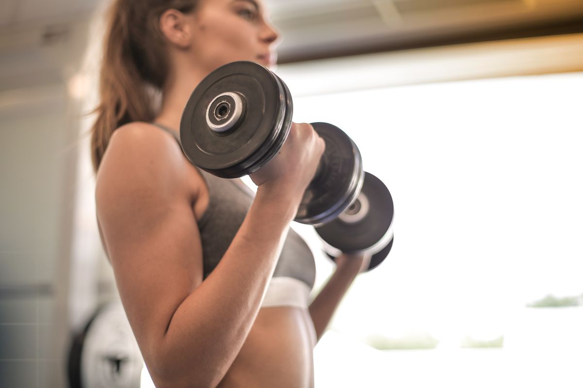 A member training with dumbbells on the floor of a bright gym