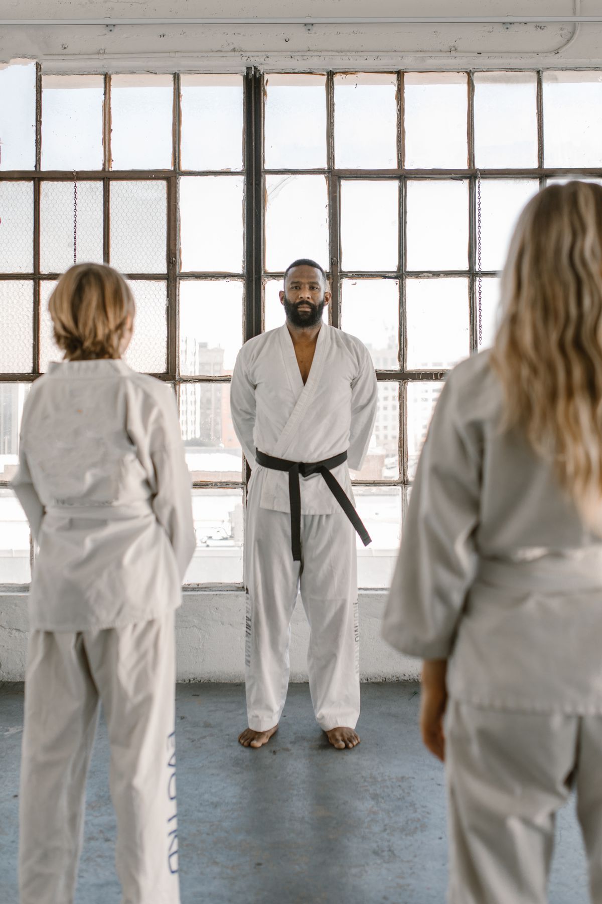 A martial arts instructor facing students at the start of a class in a bright dojo